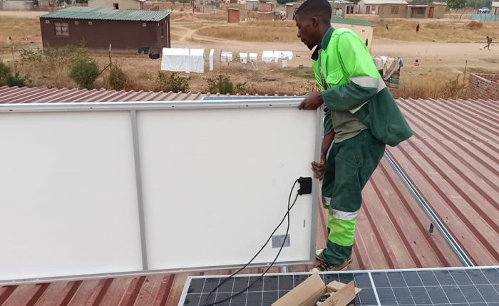 Man carefully carrying solar panels on the roof of a house