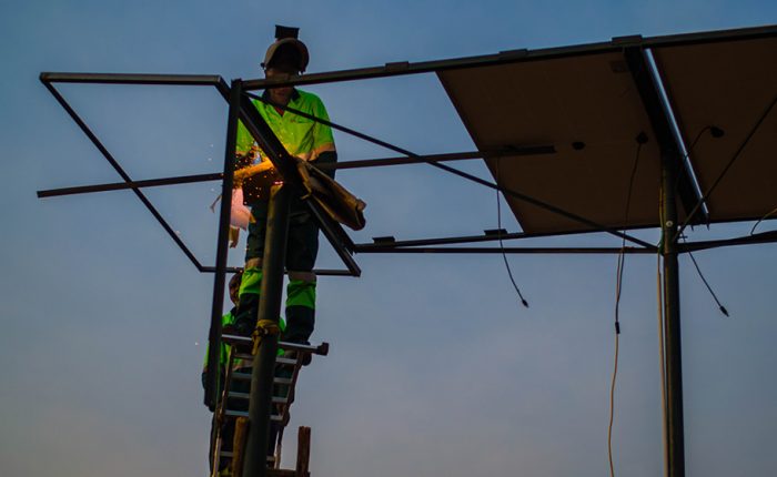 Man stand up the ladder, welding and grinding steel structure to hold solar panels